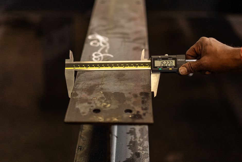 Worker measuring a steel beam with a digital caliper