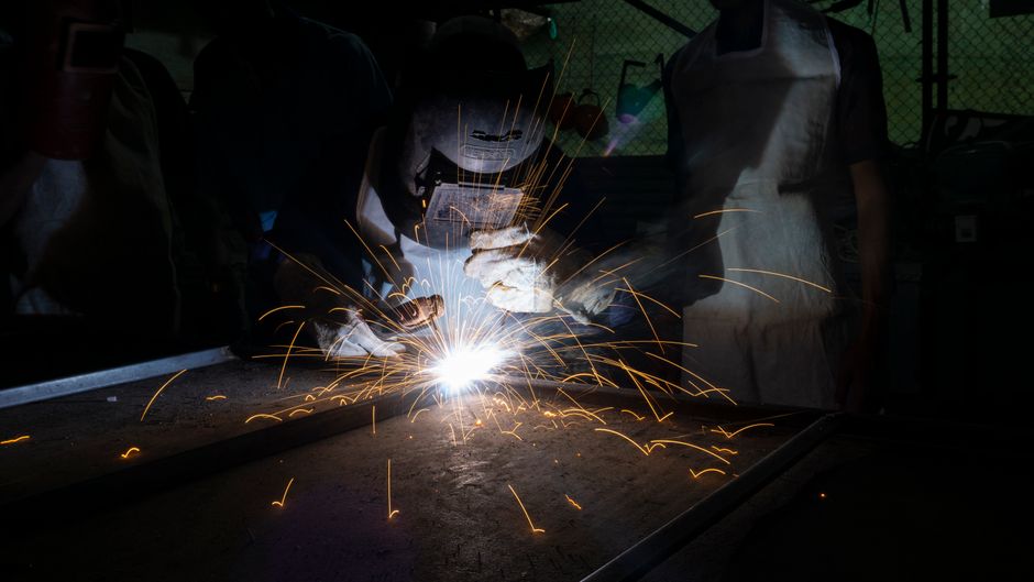 Welder in protective gear in a dark workshop